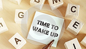 Wooden cubes with letters of the alphabet, a piece of paper with the text Â Â TIME TO WAKE UP in the middle on a wooden table